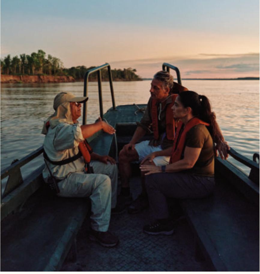 Guests and a guide aboard a small skiff on a still Amazon river at sunset